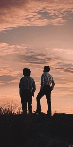 two men standing on top of a hill at sunset with the sky in the background