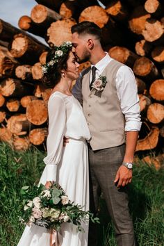 a bride and groom standing next to each other in front of stacked logs at their wedding