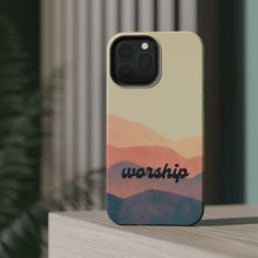 a phone case with the word worship on it sitting on a table next to a potted plant