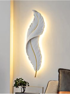 a white wall mounted with a light that has a large feather on it's side