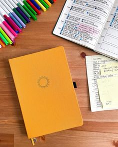 an open notebook sitting on top of a wooden table next to markers and pencils