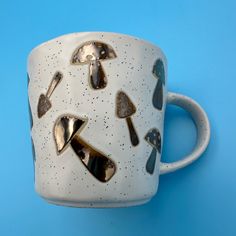 a white coffee cup with black and gold designs on it's side, against a blue background