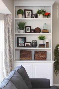 a living room filled with furniture and lots of plants on top of white bookshelves