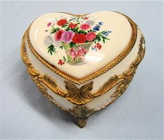 a heart shaped trinket box with flowers painted on the inside and gold trimmings