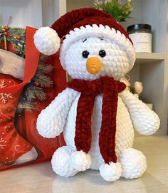 a crocheted snowman sitting next to a christmas present bag on a counter