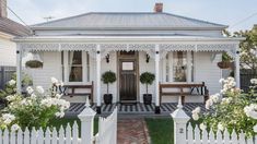 a white house with black and white checkered flooring on the front porch, surrounded by greenery