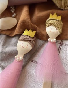 two wooden dolls with crowns on top of a bed next to pillows and other items