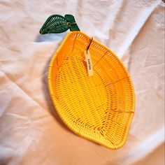 a yellow basket sitting on top of a white sheet covered floor next to a green leaf