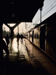 people are walking on the platform next to a train at sunset or sunrise, in silhouette