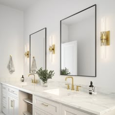 a bathroom with two sinks, mirrors and gold fixtures on the wall above them is a plant in a vase