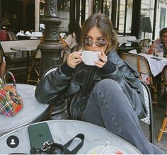 a woman sitting at an outdoor table drinking coffee