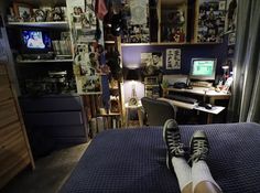 a person's feet resting on the edge of a bed in front of a computer desk