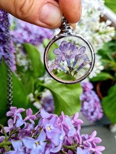 a hand holding a glass pendant with purple flowers in it