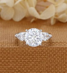 an engagement ring with three stones on top and flowers in the background, sitting on a wooden box