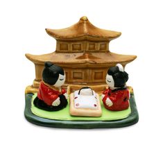 two small figurines sitting on top of a green mat with a pagoda in the background