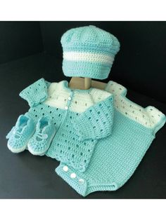 a crocheted baby outfit and booties on a black surface with a doll's hat