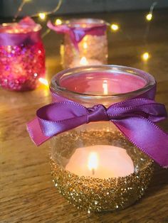 some candles are sitting on a table with lights in the background and one candle has a purple ribbon around it