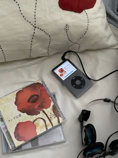 an mp3 player and headphones are on a bed next to a pillow with red flowers