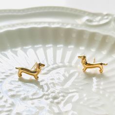 pair of gold toned dachshund earrings on white plate