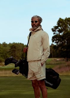 a man standing on top of a green field holding a golf racquet and bag