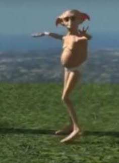 an alien standing in the grass with its arms outstretched and legs spread out, wearing a hat