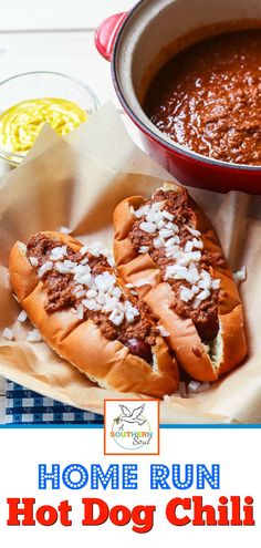 two hot dogs in buns with chili and cheese on the side next to a bowl of soup