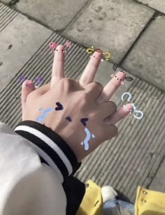 someone has their fingers painted with different colors and shapes on them while sitting on the sidewalk