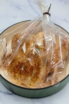 some chicken wrapped in plastic sitting on top of a pan filled with meat and seasoning