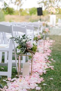 the aisle is lined with white chairs and pink petals on the grass, as well as greenery