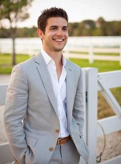 a man standing in front of a white fence wearing a gray suit and tan pants