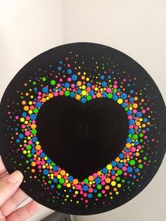 a hand holding up a black plate with colorful dots on the inside and in the shape of a heart