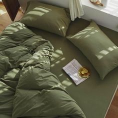 an unmade bed with green sheets and pillows on it, next to a window