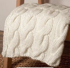 a white knitted blanket sitting on top of a wooden chair