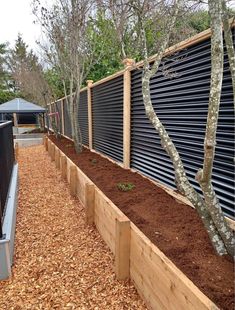 a wooden fence is lined with mulch and trees