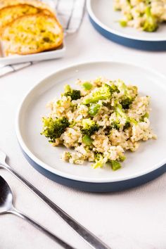 two plates with rice and broccoli on them next to silverware, bread and utensils