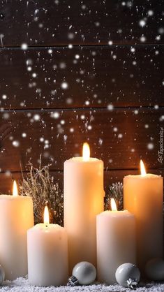 lit candles in front of snow falling on the ground with christmas decorations and ornaments around them