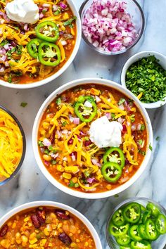 several bowls filled with chili, beans and cheese on a marble counter top next to green peppers