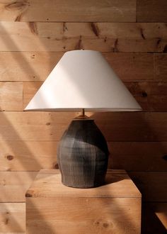 a lamp sitting on top of a wooden table next to a wall covered in wood planks