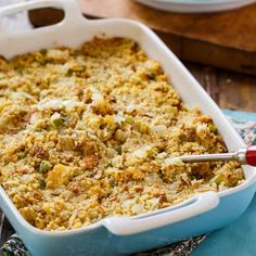 a blue casserole dish filled with stuffing and topped with a red spatula