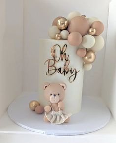 a teddy bear sitting on top of a white cake with gold and white balloons around it