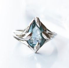 a white gold ring with an aqua blue topazte stone in the center, on a white background