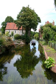 two people in a small boat traveling down a narrow river surrounded by trees and houses