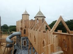 a wooden castle with a slide and play area in the back ground, surrounded by wood planks