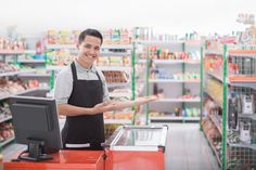 a man standing in front of a cash register at a grocery store holding out his hand