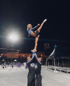 two cheerleaders doing acrobatic tricks in front of a crowd at night