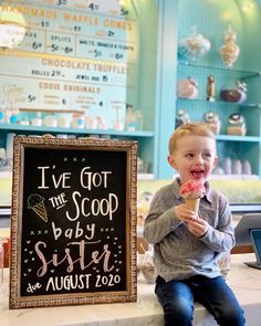 a little boy sitting on top of a counter eating an ice cream cone in front of a chalkboard sign