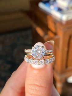 a woman's hand holding a diamond ring with two wedding bands on top of it