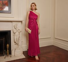 a woman standing in front of a fireplace wearing a pink dress and holding a purse