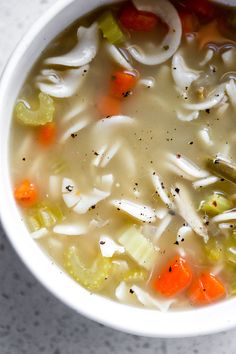 a white bowl filled with chicken noodle soup next to carrots and celery