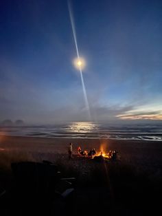 people sitting around a campfire on the beach at night